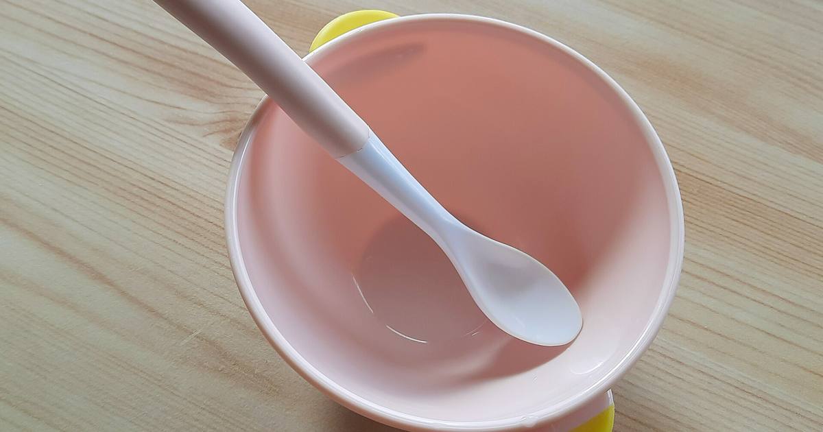 Chiếc bát và thìa mềm màu hồng dành cho bé tập ăn dặm đặt trên mặt bàn gỗ